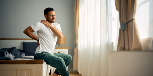 Man holding back and shoulder sitting on the edge of a bed 