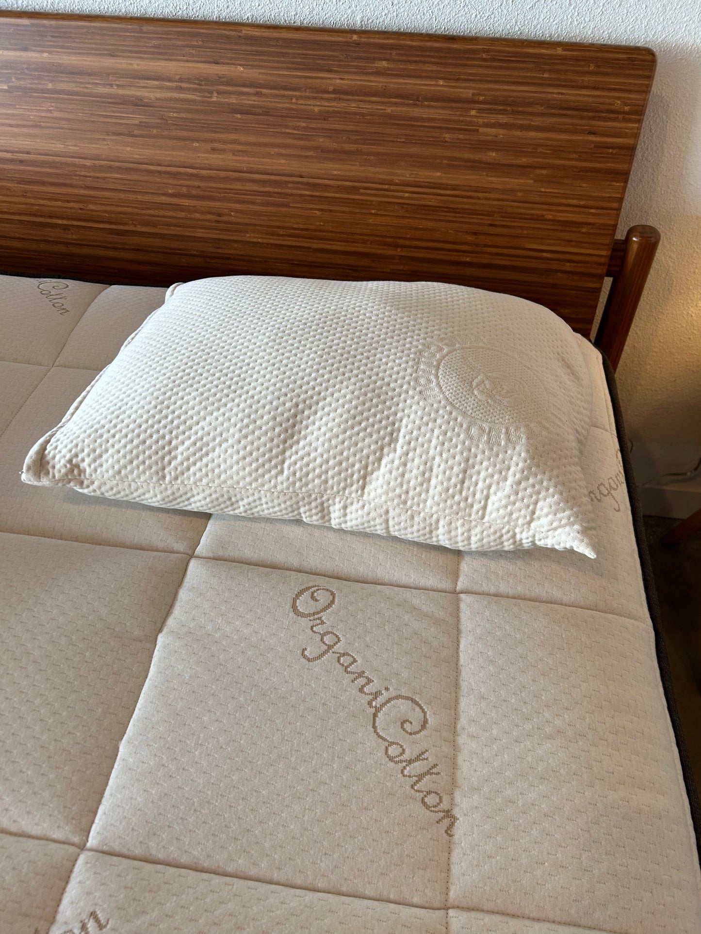 White pillow on beige mattress with wooden headboard